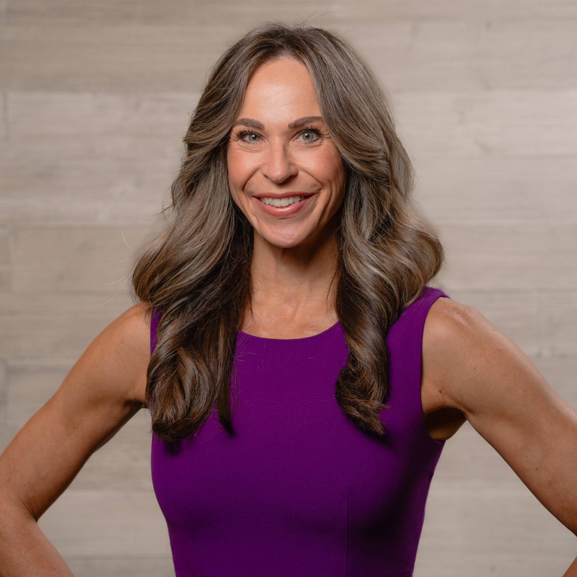 Woman in a purple dress smiling against a neutral background