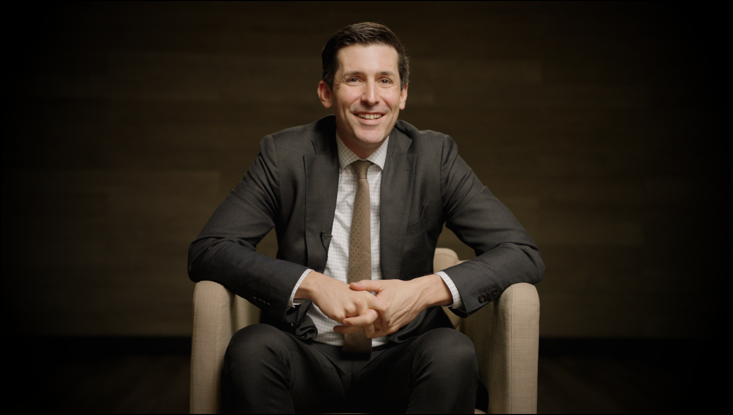Man in a suit sitting on a chair against a dark background