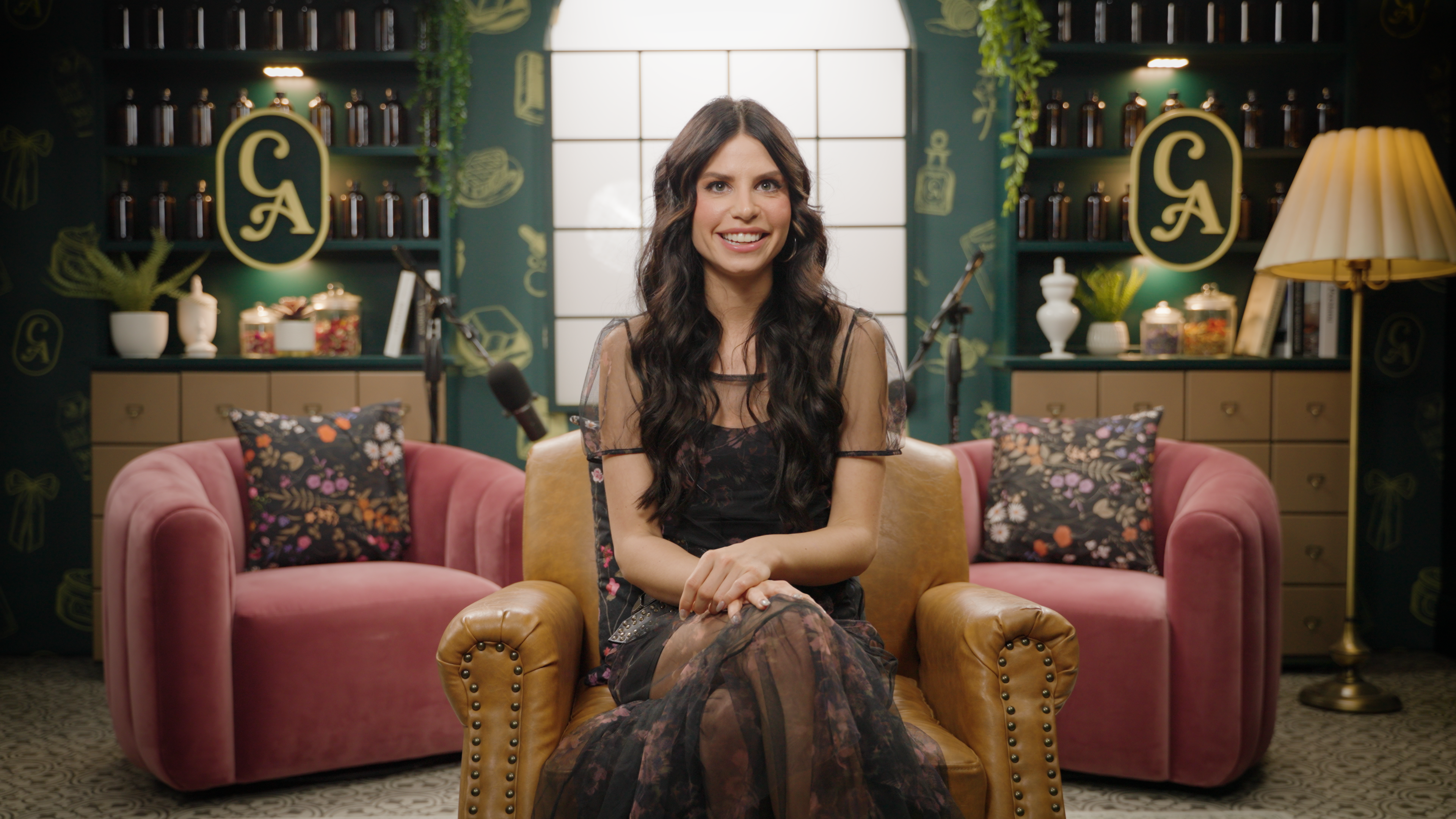 Woman sitting in a stylish room with pink chairs and decorative elements.