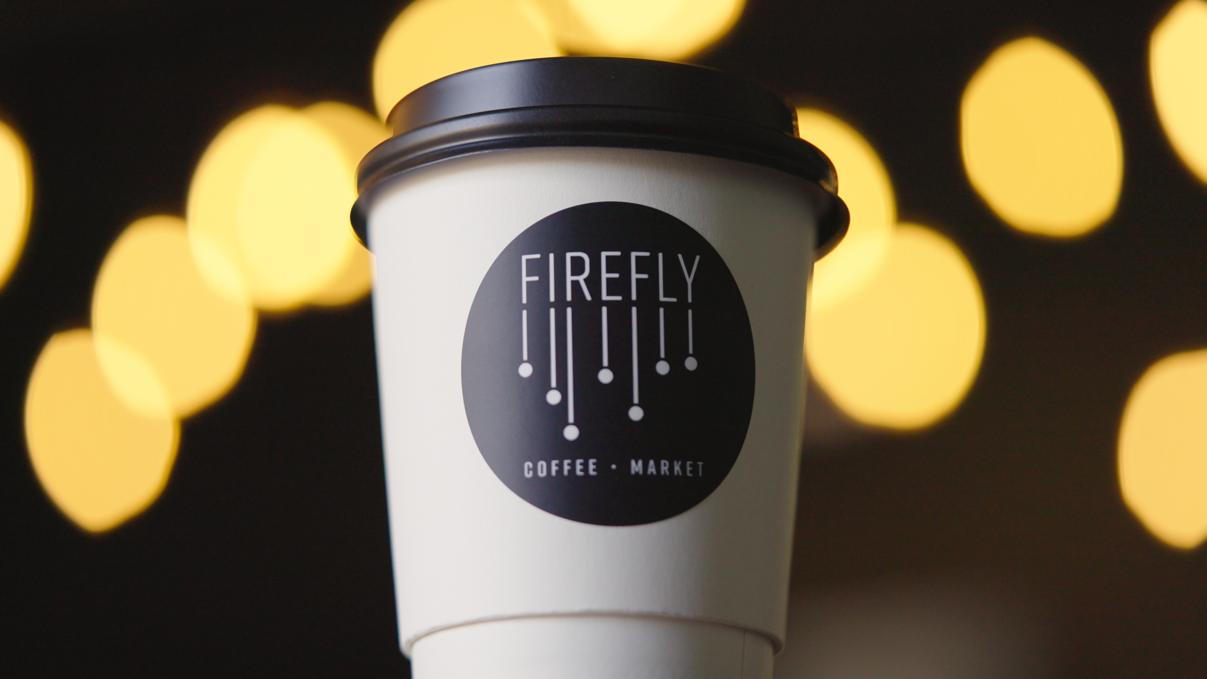 White coffee cup with 'Firefly Coffee & Market' logo against a blurred bokeh background