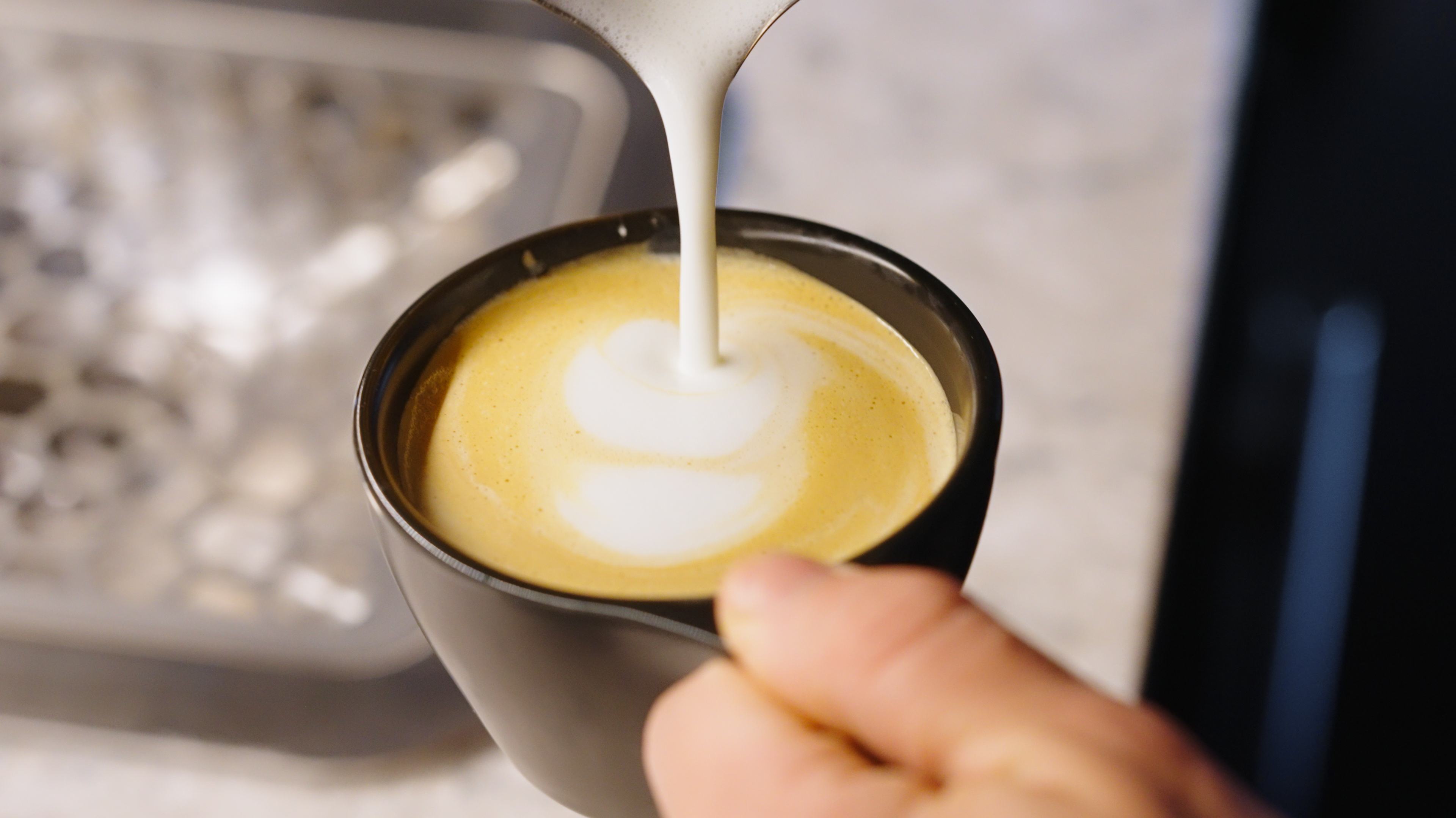 Person pouring milk into a cup of coffee to create latte art.