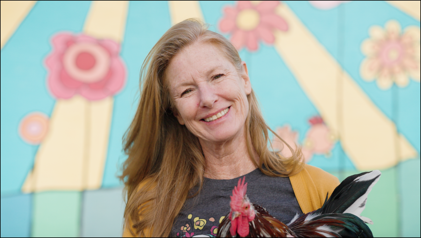 Woman holding a rooster in front of a colorful abstract background