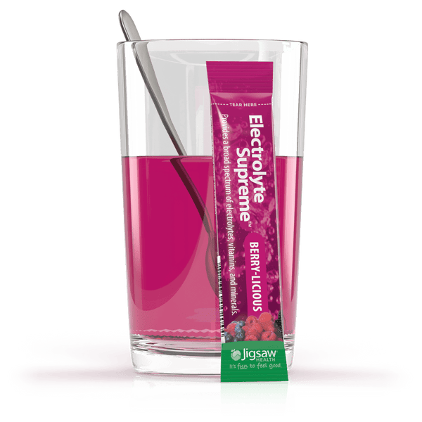 Jigsaw Electrolyte Supreme berry-licious packet in front of glass of water with matching powder mixed in.
