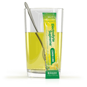 Glass of lemon-lime flavored drink with a Jigsaw Electrolyte Supreme lemon-lime flavor packet.