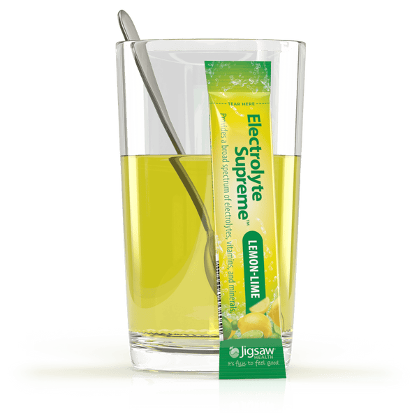 Glass of lemon-lime flavored drink with a Jigsaw Electrolyte Supreme lemon-lime flavor packet.